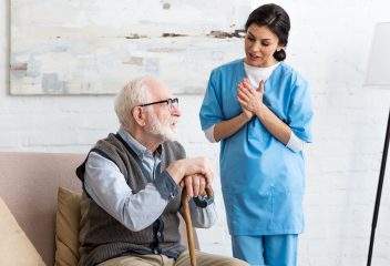 Nurse talking to bearded senior man, standing inside bright room