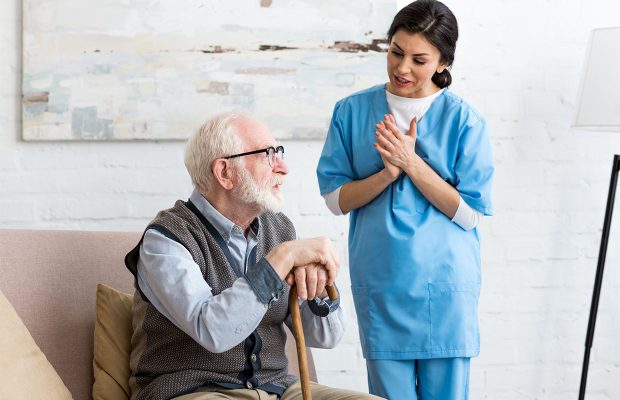 Nurse talking to bearded senior man, standing inside bright room